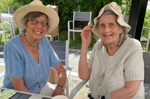 Två boende sitter på uteplats i solhatt.